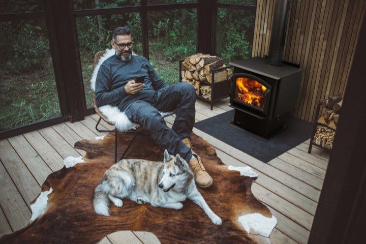 Quadra-Fire wood stove burning in a screened porch, man relaxing with his husky